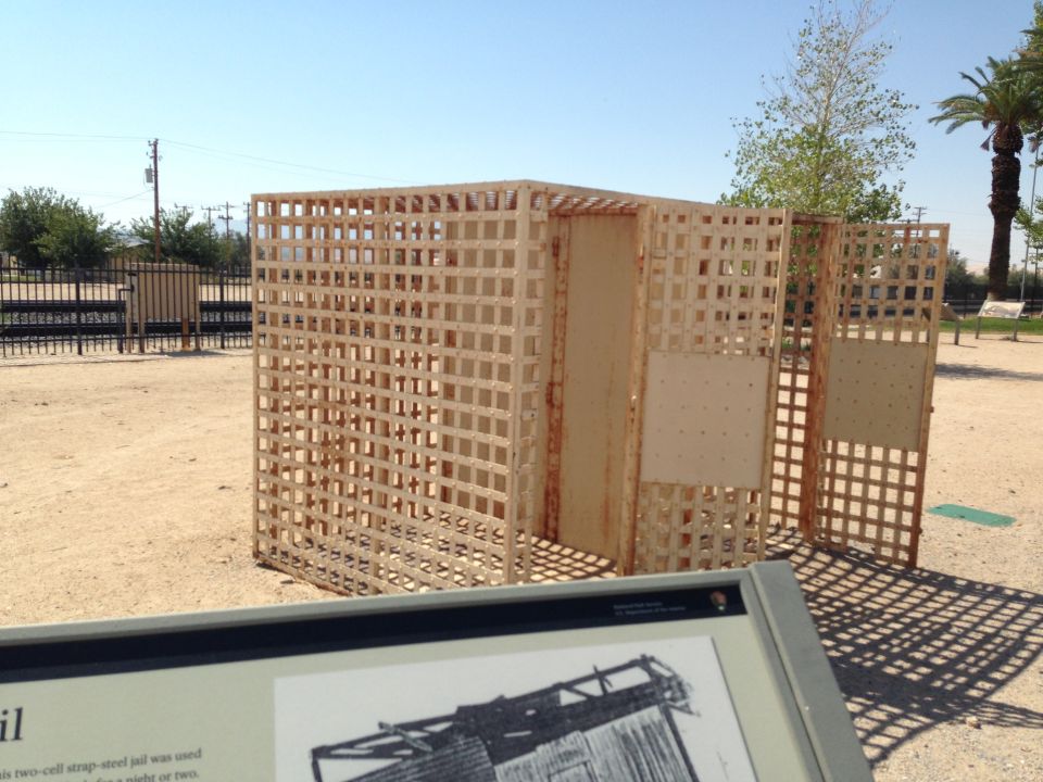 Outdoor exhibit of a two-cell jail made of wood lattice, with a sign in the foreground