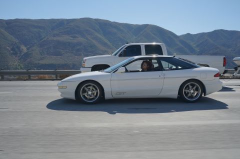 1995 Ford Taurus - A white coupe with a sunroof and GT badging drives alongside a white pickup truck on a highway.