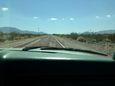 1986 Ford Bronco - View from inside a vehicle driving on a highway through a desert landscape under a clear blue sky.