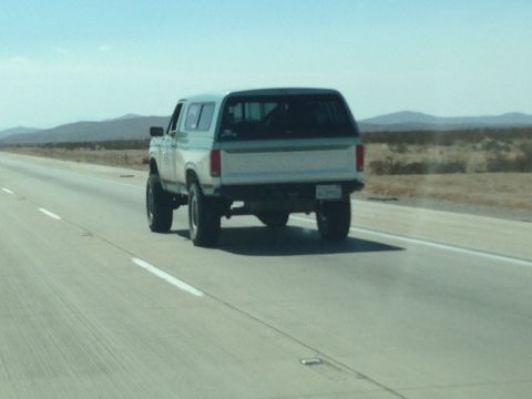 1986 Ford Bronco - Rear view of a 1986 Ford Bronco on a desert highway.