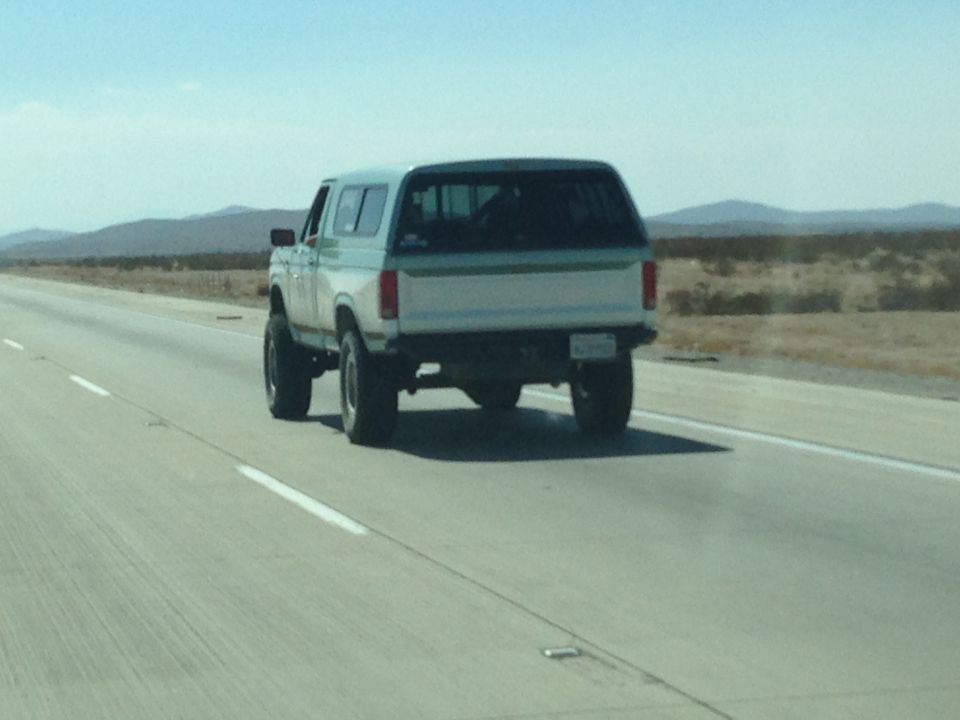 1986 Ford Bronco driving on a highway, rear view