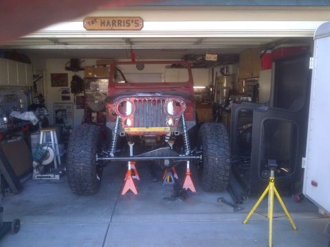 1985 Jeep CJ7 - A red Jeep CJ is in a garage, raised on jack stands with its front end partially disassembled.