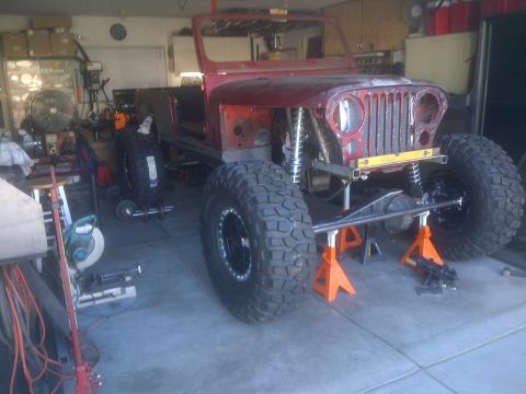1985 Jeep CJ7 - A red Jeep CJ is in a garage, partially disassembled and modified with large tires.