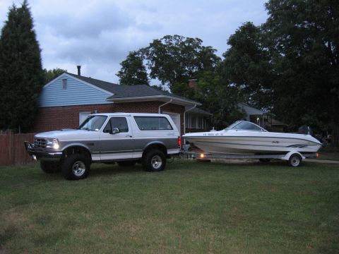 1994 Ford Bronco - A two-tone silver and grey Ford Bronco is parked on a grassy lawn, towing a white boat on a trailer.