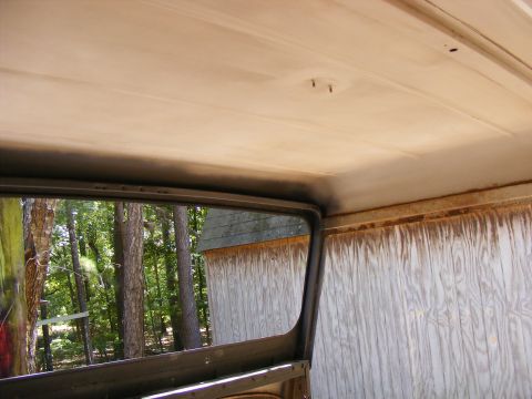 Interior view looking out a window at trees and a wooden shed. The vehicle's headliner and window frame are vi
