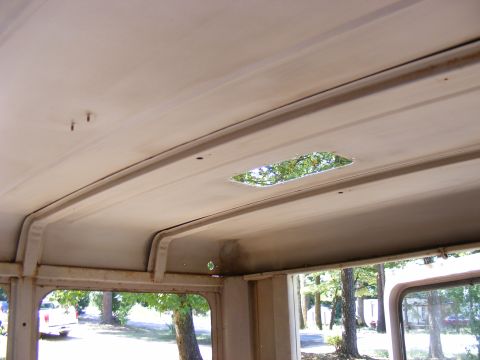 Interior ceiling of a vehicle with a rectangular opening showing trees outside. Some rust spots are visible