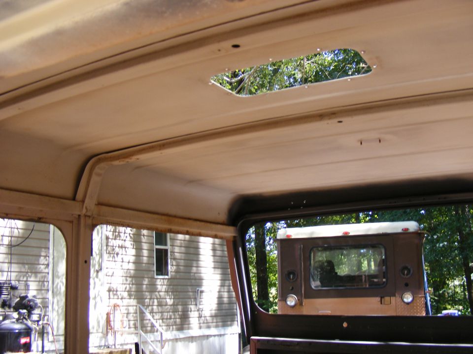Interior of a vehicle with a skylight, looking out at the rear of a brown and white SUV