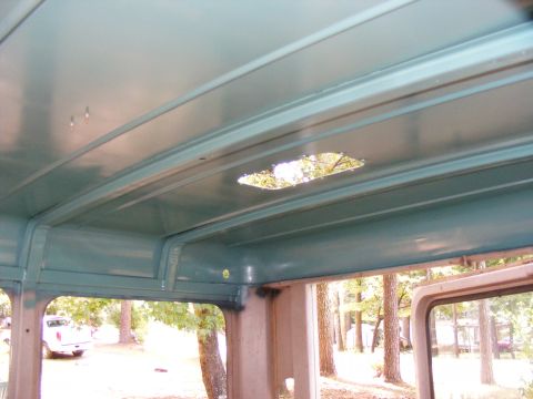 Interior view of a vehicle, showing the headliner with a hole and a white pickup truck visible through the sid
