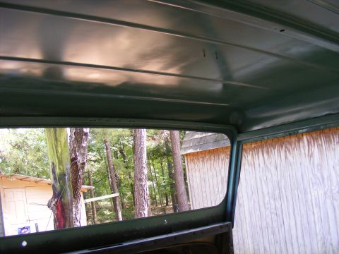 Looking out the window of a green vehicle, trees and a wooden building outside. Watermark says SUPERMOTORS.NET