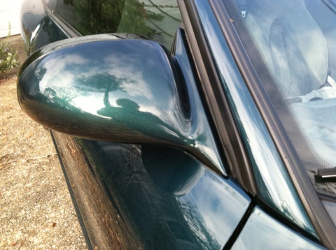 1997 Ford Probe - Side mirror and window of a green car, reflecting the sky and surrounding trees.