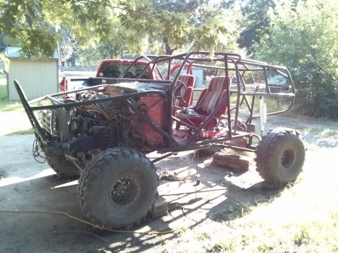 1986 Ford Bronco - A custom-built off-road buggy is shown with a roll cage and large tires, with a red pickup truck behind it.