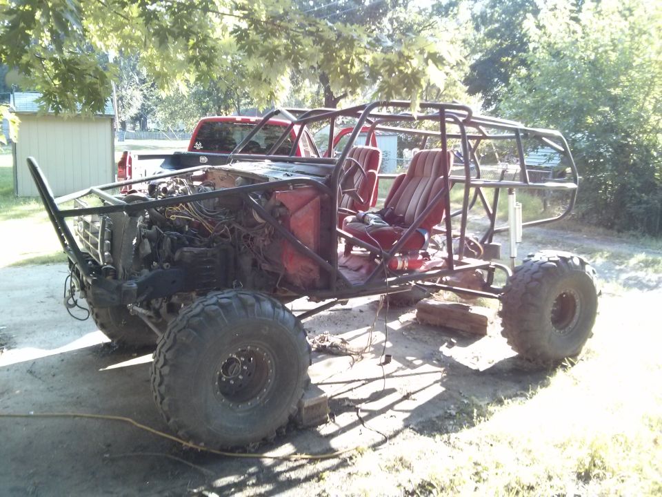 Custom buggy with roll cage, red seats, and large tires. Red pickup truck in background