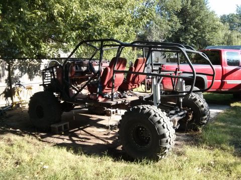 1986 Ford Bronco - A heavily modified off-road vehicle with a custom roll cage and large tires sits in a yard.