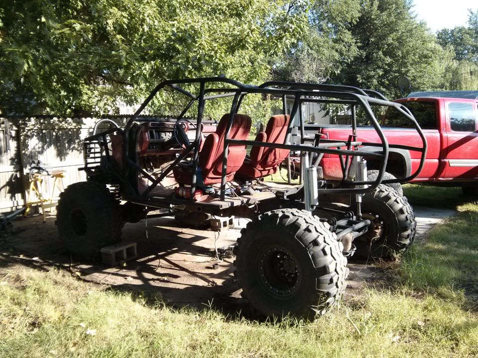 Custom off-road buggy with red seats and roll cage, parked outdoors next to a red pickup truck