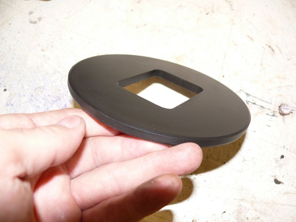 Black oval automotive part with a square cutout, held by a hand