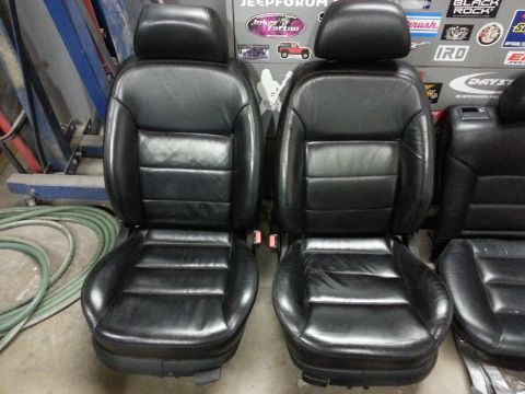 2002 Volkswagen Jetta - Two black leather car seats are displayed in front of a wall with various stickers and a green hose coiled on the floor.
