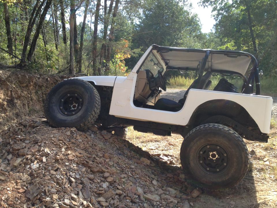 White Jeep Wrangler with large tires on a rocky incline, soft top up, doors removed