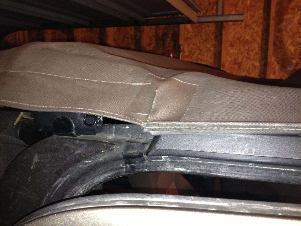 Close-up of a torn soft top on a vehicle, with tape applied to a rip. Shows the seam and attachment points