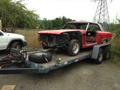 1964 Ford Fairlane - A red coupe project car is being transported on a trailer, stripped down and ready for restoration.