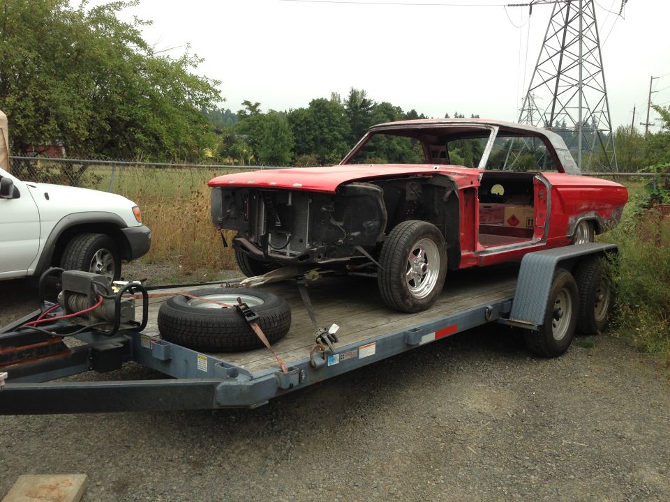 Red coupe project car on trailer, missing hood, fenders, and interior components