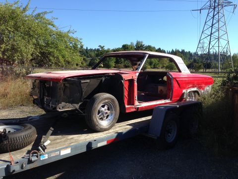 1964 Ford Fairlane - A red 1964 Ford Fairlane body sits on a trailer, awaiting restoration under a clear blue sky.