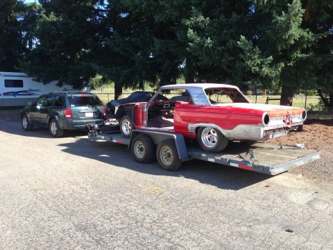1964 Ford Fairlane - A red classic car body, missing its front end and interior, is transported on a trailer.