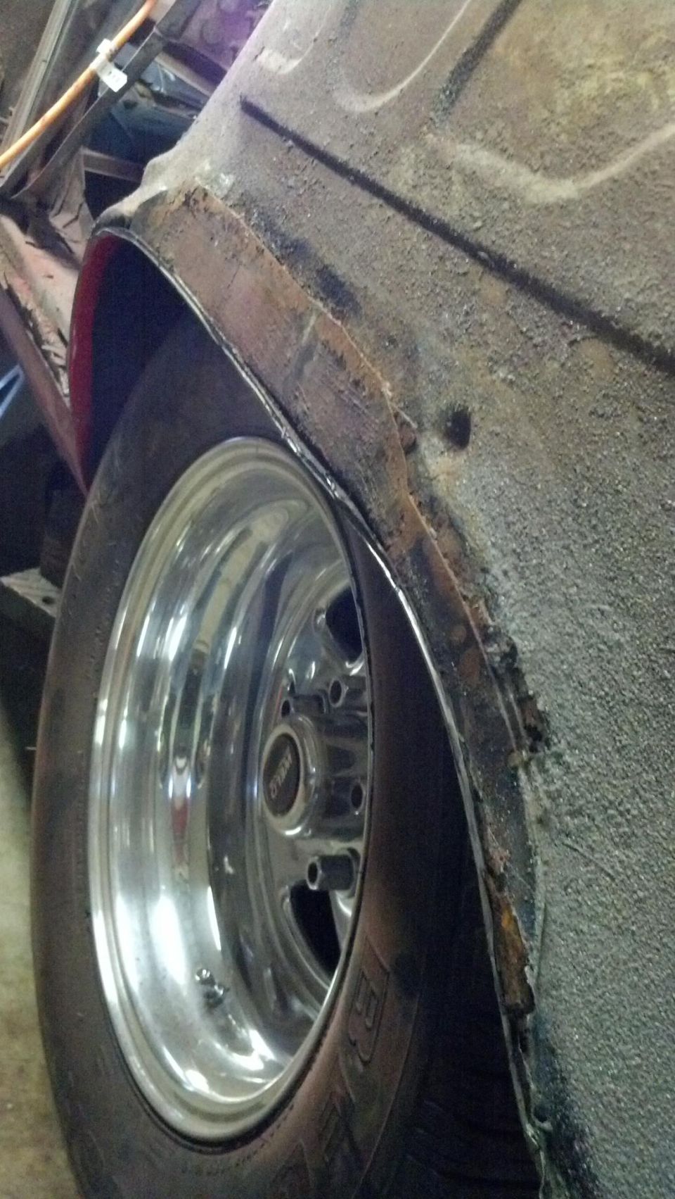 Chrome five-spoke wheel and tire in rusty wheel well of a car