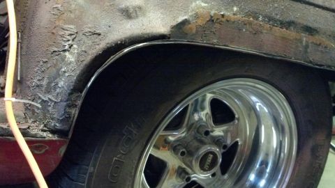 1964 Ford Fairlane - Close-up of a rusty rear wheel well and a chrome rim on a vehicle.