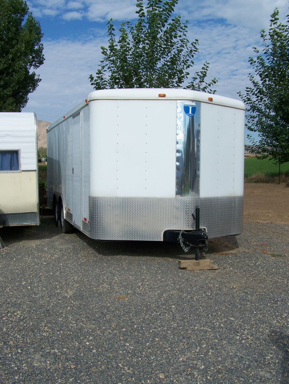 White enclosed trailer with diamond plate lower front, parked next to a smaller trailer