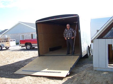 1988 Suzuki Samurai - A red pickup truck is seen towing a trailer, positioned near a large, open cargo trailer with a man standing inside.