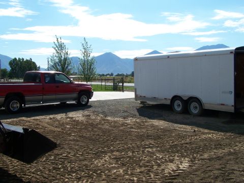 1988 Suzuki Samurai - A red pickup truck is parked beside a white trailer in a rural setting with mountains in the background.