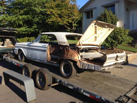 1964 Ford Fairlane - A white 1964 Ford Fairlane coupe, in a state of disrepair, is loaded onto a trailer for transport.