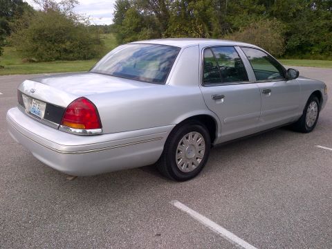 2001 Ford Crown Victoria - A silver 2001 Ford Crown Victoria sedan is parked on an asphalt surface with trees in the background.