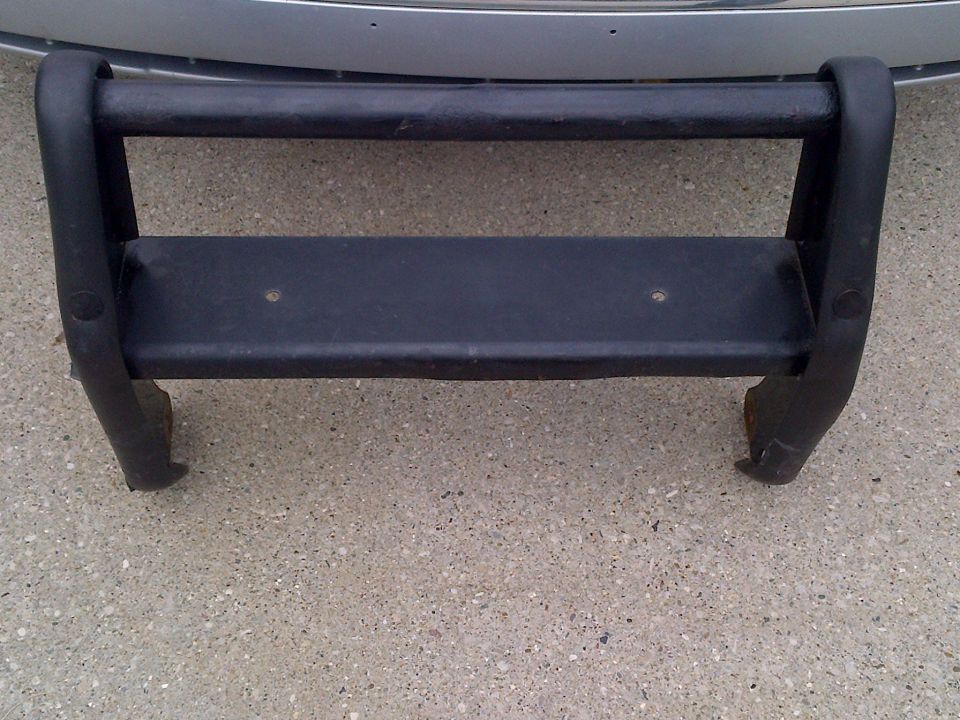Black bull bar with two horizontal bars and a flat step, mounted on concrete