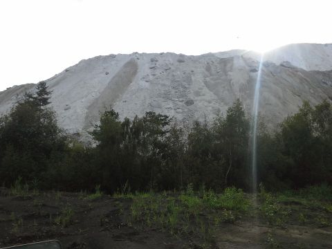 1987 Ford Bronco - A large sand pile dominates the background, with trees in the foreground and a sun flare.