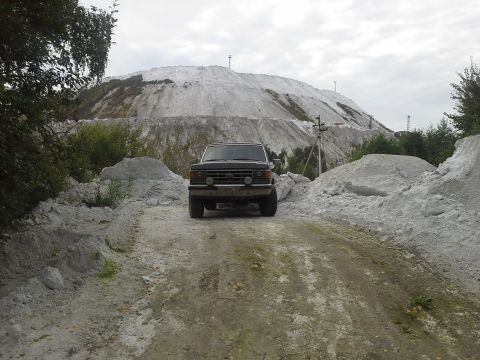 1987 Ford Bronco - SUV parked on a dirt road with a large white hill behind it. Grille suggests an early 1980s model.