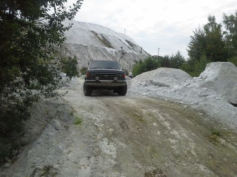1987 Ford Bronco - A 1987 Ford Bronco navigates a dusty, off-road path with large mounds of white material in the background.