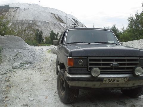 1987 Ford Bronco - A dark SUV is parked on a dirt road, with a large white hill in the background.