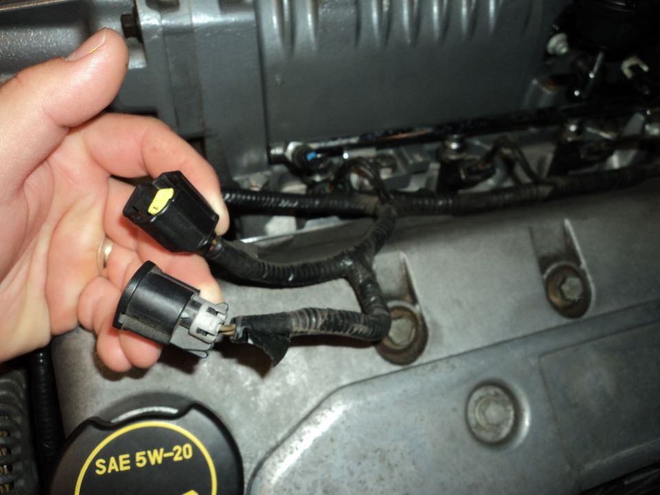 Hand holding engine wiring connectors near SAE 5W-20 oil cap