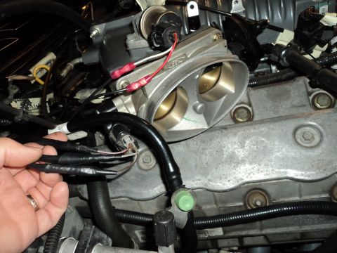 2004 Mercury Grand Marquis - Close-up of engine bay components, including a throttle body and wiring harness, with a hand present.