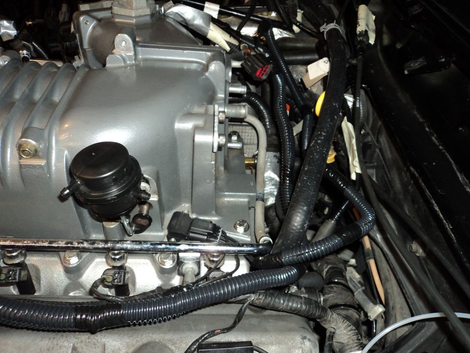 engine bay with a silver supercharger, black hoses, and wiring