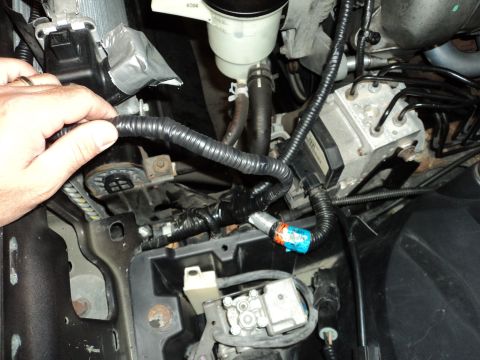 2004 Mercury Grand Marquis - Close-up of engine bay components, including wiring, ABS module, and fluid reservoir, with a hand adjusting wiring.