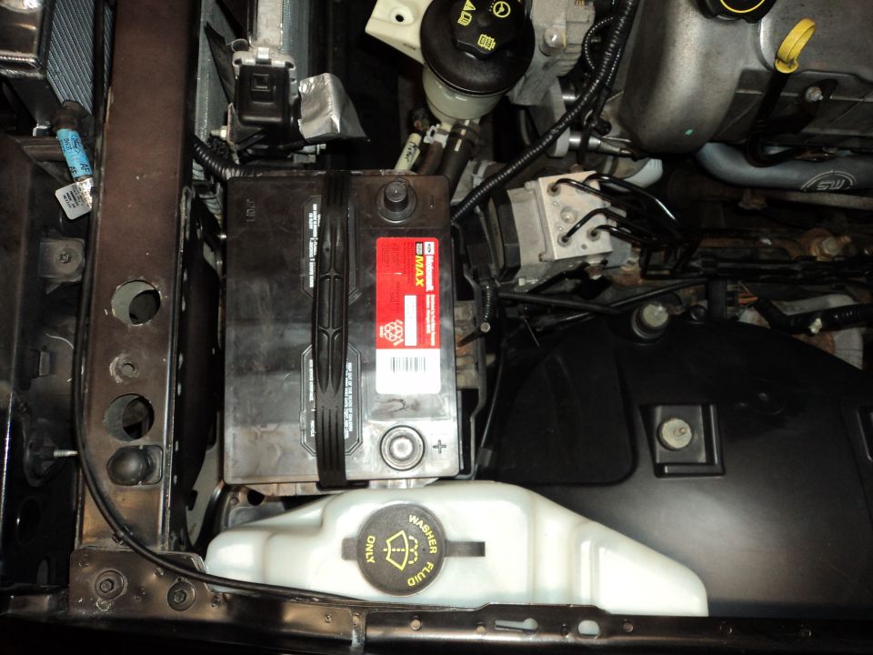 Engine bay showing a car battery, washer fluid reservoir, and various engine components