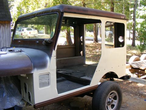 Jeep CJ-5 body with doors removed, undergoing restoration. It's sitting on a trailer outside