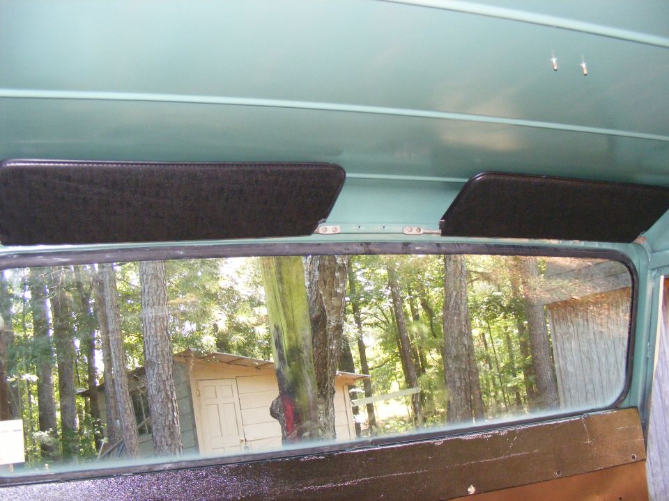 Interior view of a teal vehicle showing two black sun visors and a rear window reflecting trees and a small building