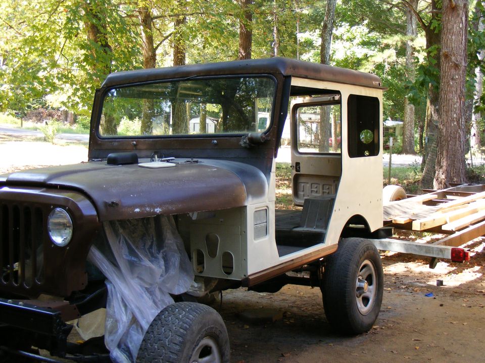 Jeep CJ-5 body with no engine, doors open, sitting on a trailer frame
