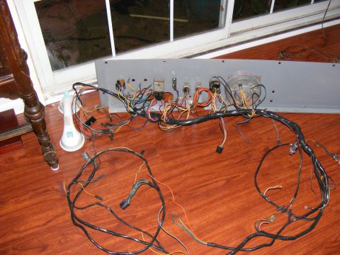 Vehicle wiring harness spread out on a wooden floor with a dashboard panel and gauges