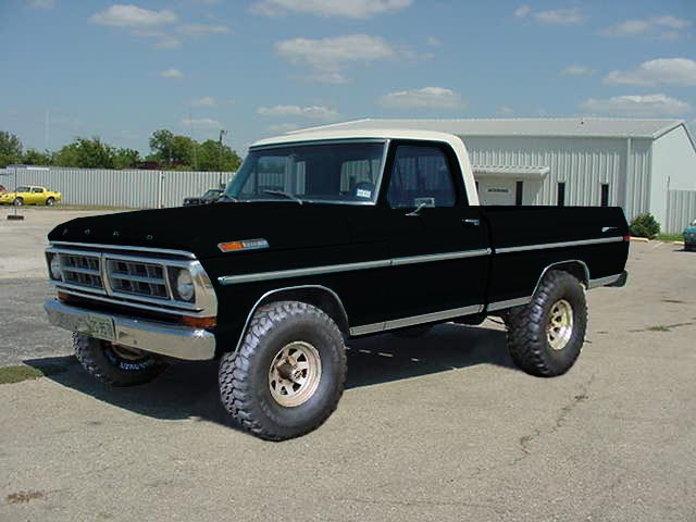 Black Ford pickup truck with white roof and large tires parked on asphalt