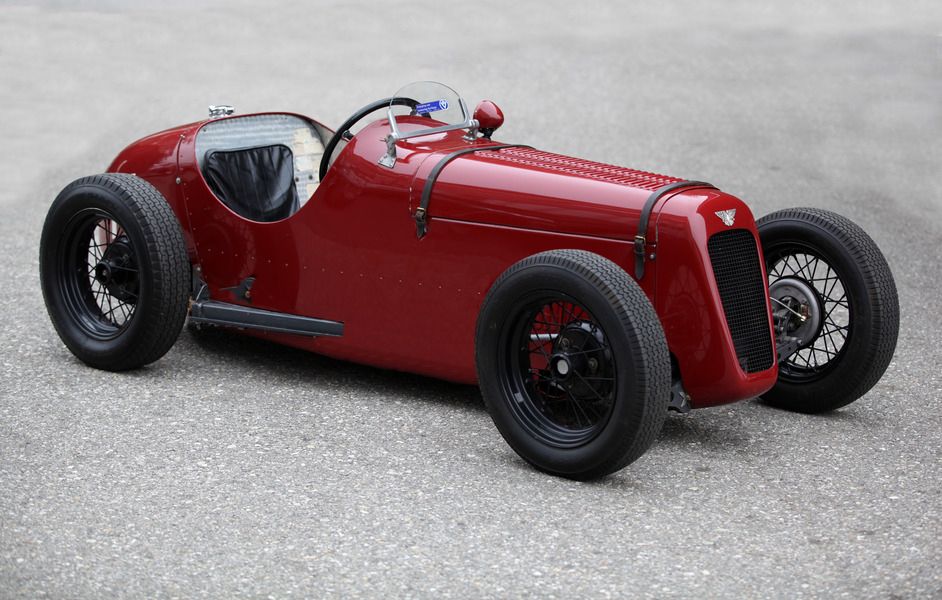 Red vintage race car with black wire wheels and black leather interior, viewed from the front three-quarter angle