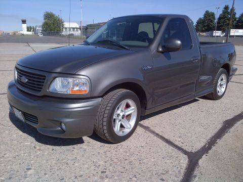 2003 Ford F-150 - A dark gray Ford F-150 Lightning pickup truck is parked on a paved surface with a building and trees in the background.